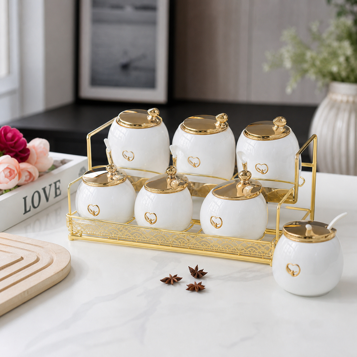 White ceramic canisters with knobbed gold lids and serving spoons on a gold-tone rack, on a counter
