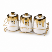 Three white ceramic canisters with gold drip-glaze lids on a gold-tone wire rack