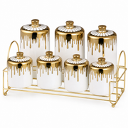 Seven white ceramic spice jars with gold drip-glaze lids on a gold-tone rack