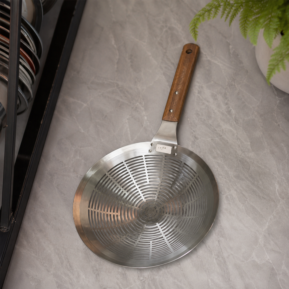Perforated stainless steel plate with wooden handle lying on a grey marble kitchen worktop