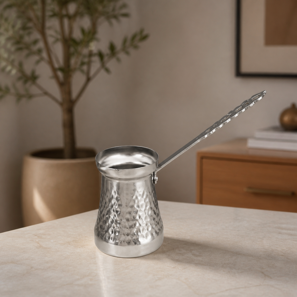 Long-handled hammered stainless steel coffee pot with open top, on a marble table