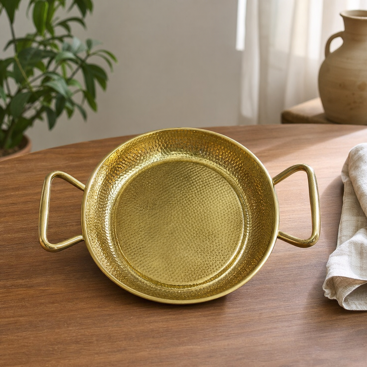 Hammered gold-tone serving pan with two open loop handles, on a wooden table