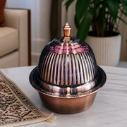 Copper-tone covered serving bowl with ribbed domed lid and finial, on a marble table