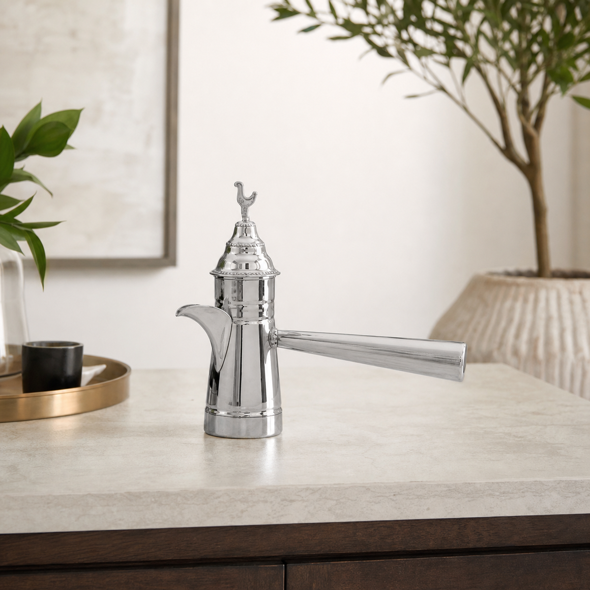 Polished silver coffee pot with long side handle on a kitchen counter