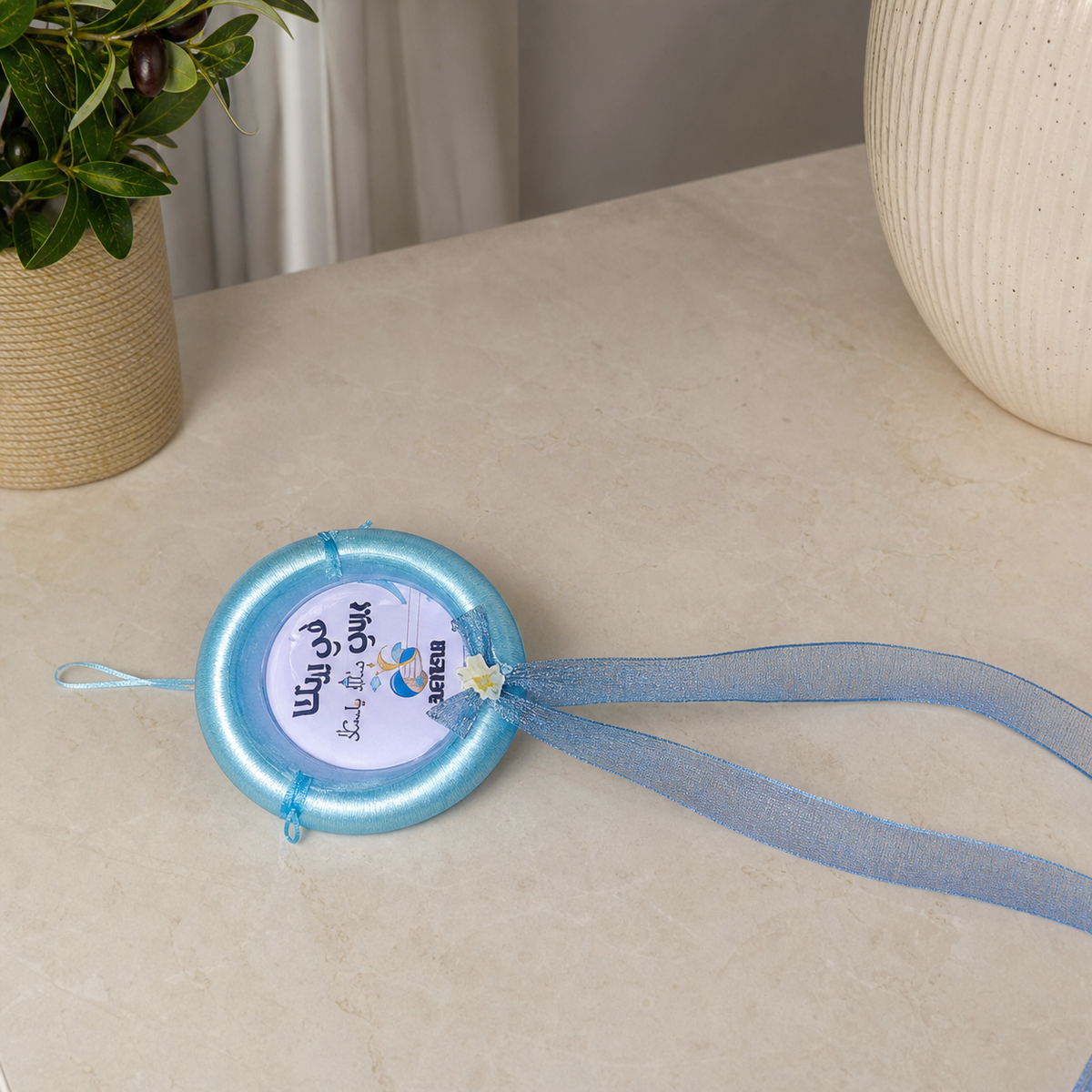 Light blue satin hoop decoration with organza bow, cream flower and streamers, printed card at centre