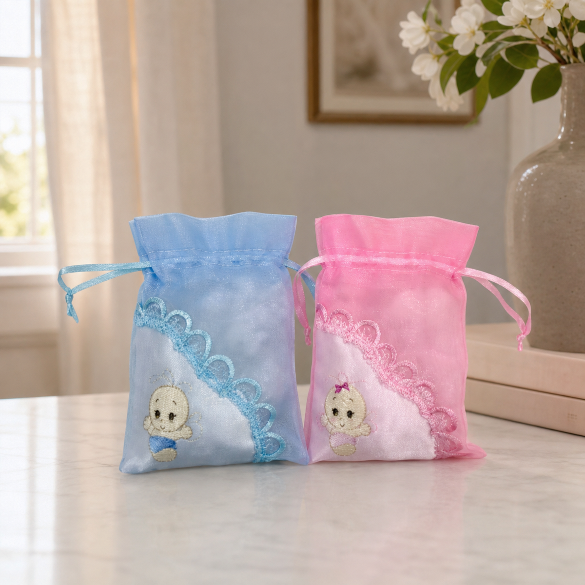 Pink and blue organza baby favor pouches with drawstrings on a marble table
