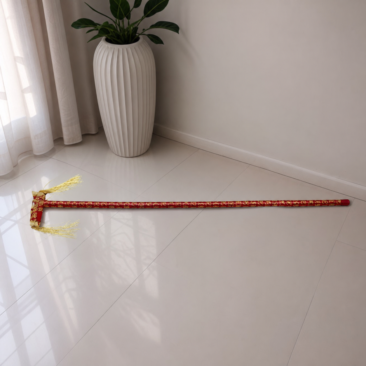 Red celebration cane with gold pattern and two pale tassels, shown on a tiled floor