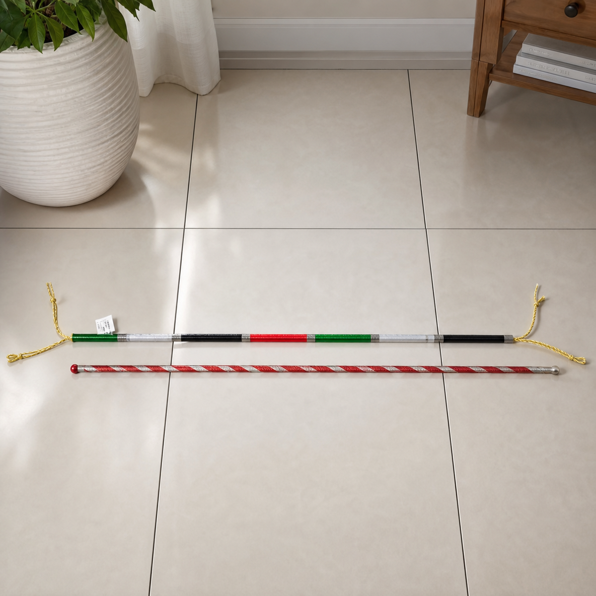 Two decorative celebration sticks lying on a tiled floor beside a white plant pot