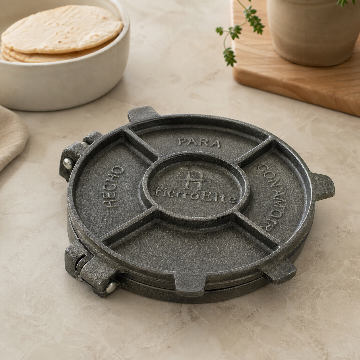 Hinged dark grey cast metal tortilla press on a kitchen counter beside a bowl of tortillas