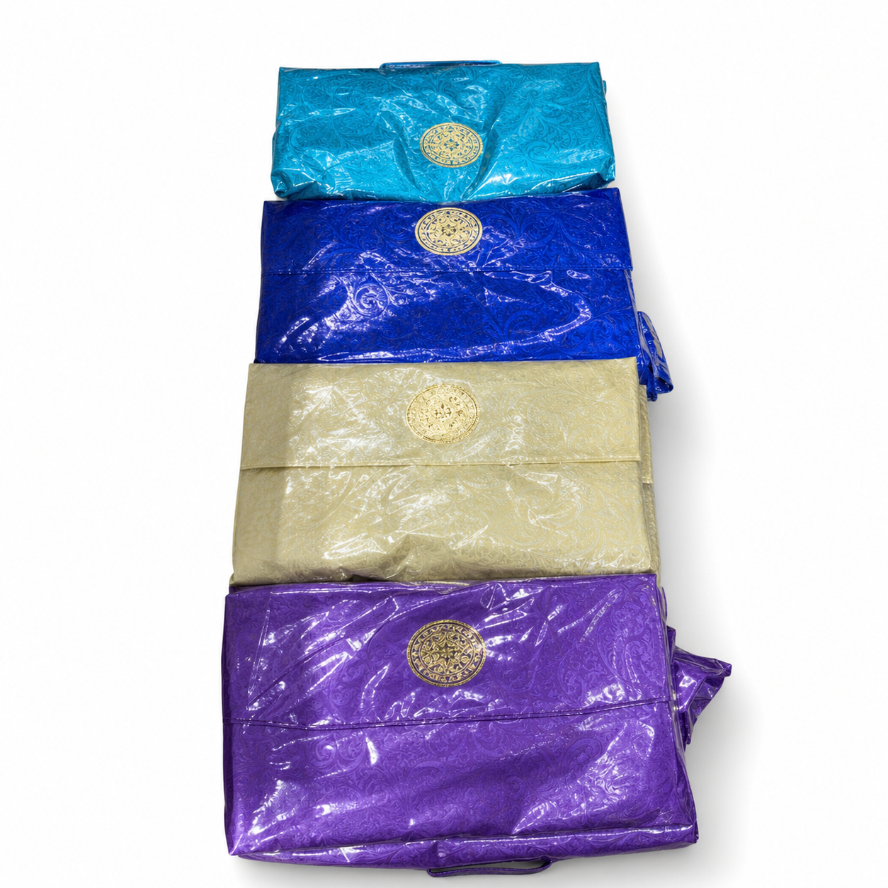 Four wrapped blankets stacked: light blue, royal blue, cream and purple, each with a gold medallion