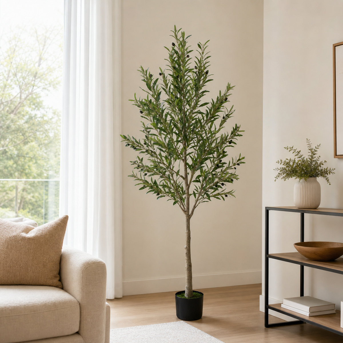 Living-room scene: tall artificial olive tree in a black planter, canopy carrying dark olives