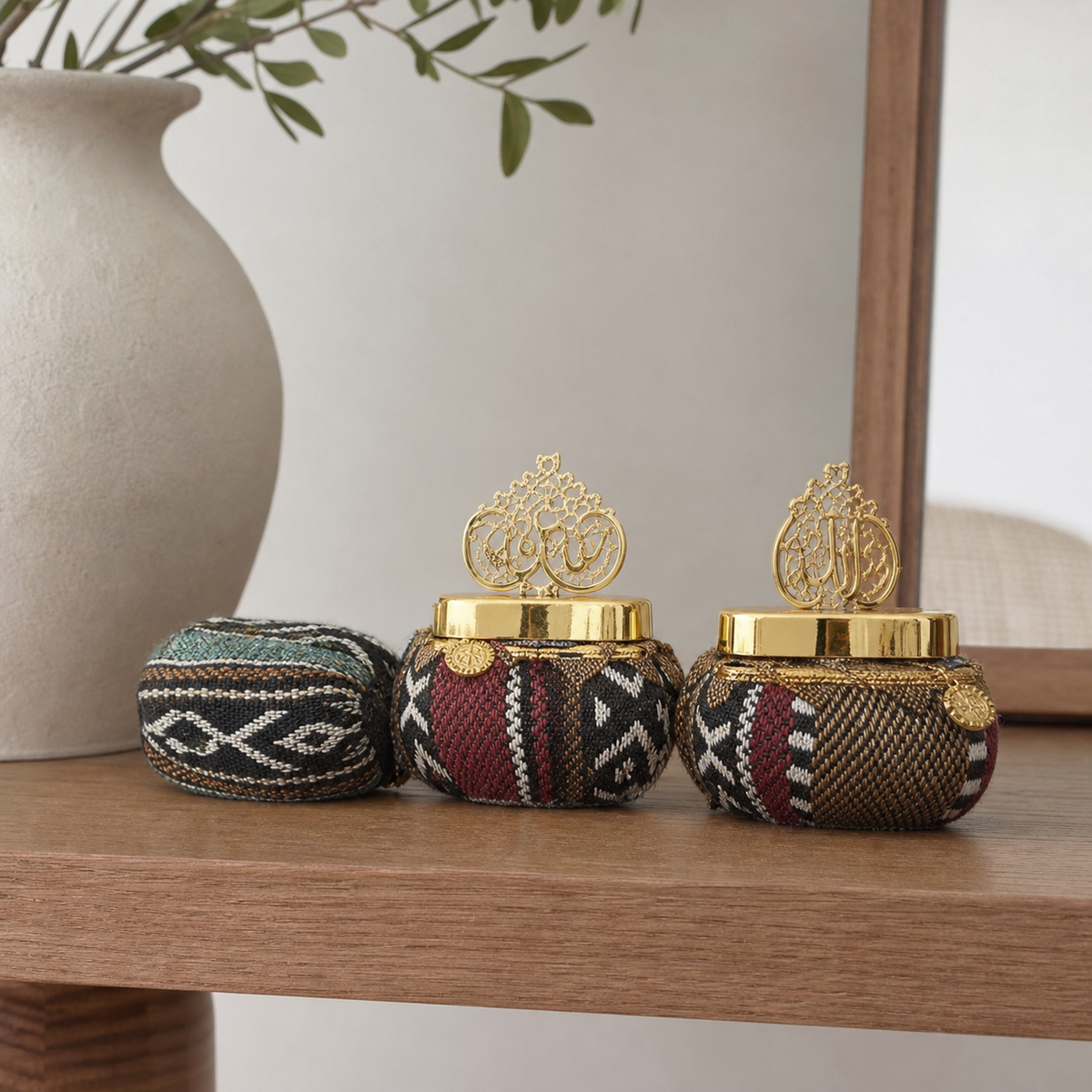 Three patterned fabric-covered favor pots with gold-tone lids on a wooden console table