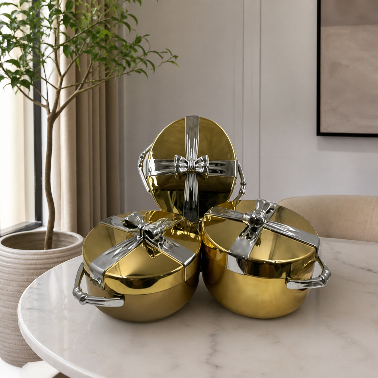 Gold casserole warmer set of three on a marble table, silver bow detail on each lid