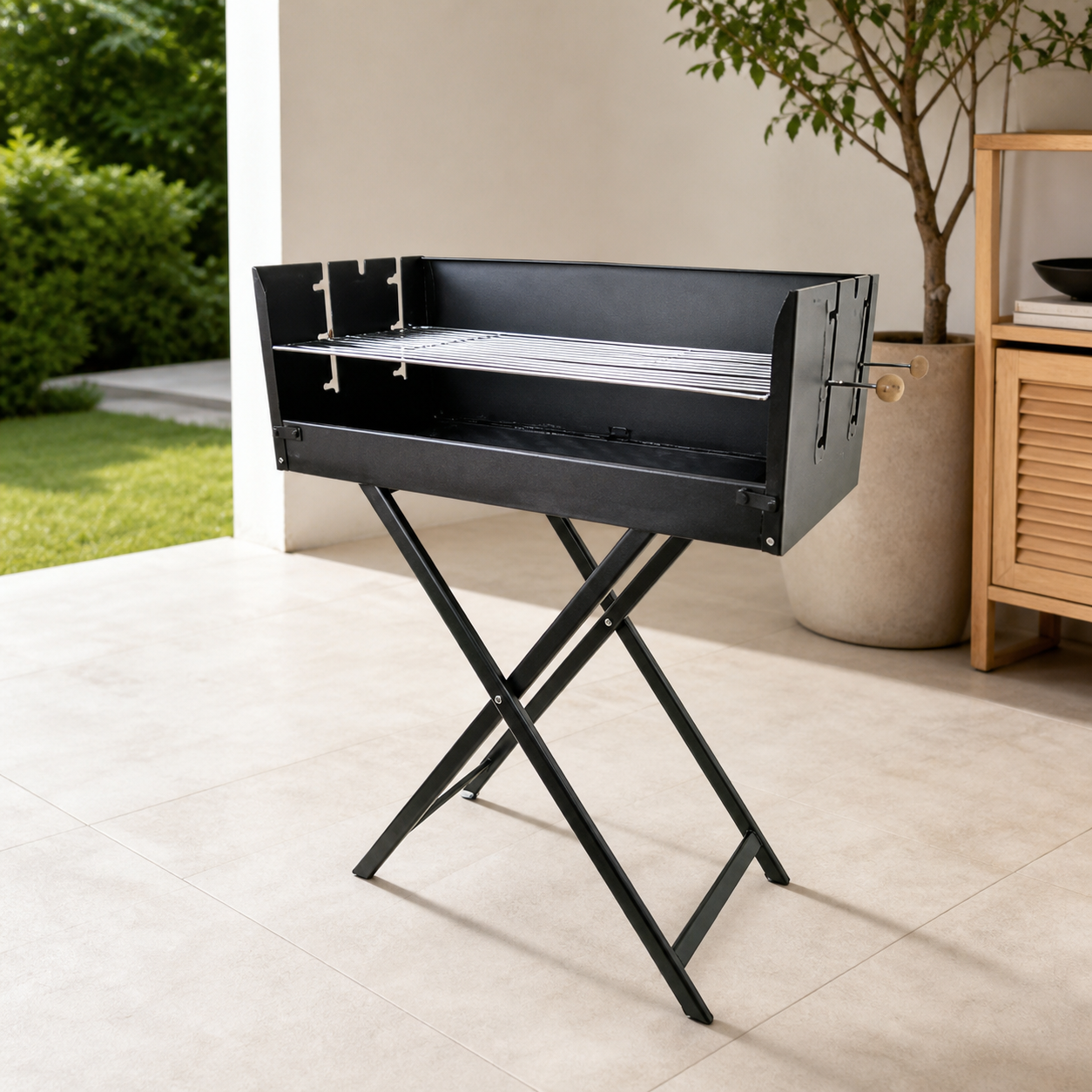 Black folding charcoal grill on an X-frame stand, on a patio beside a planter