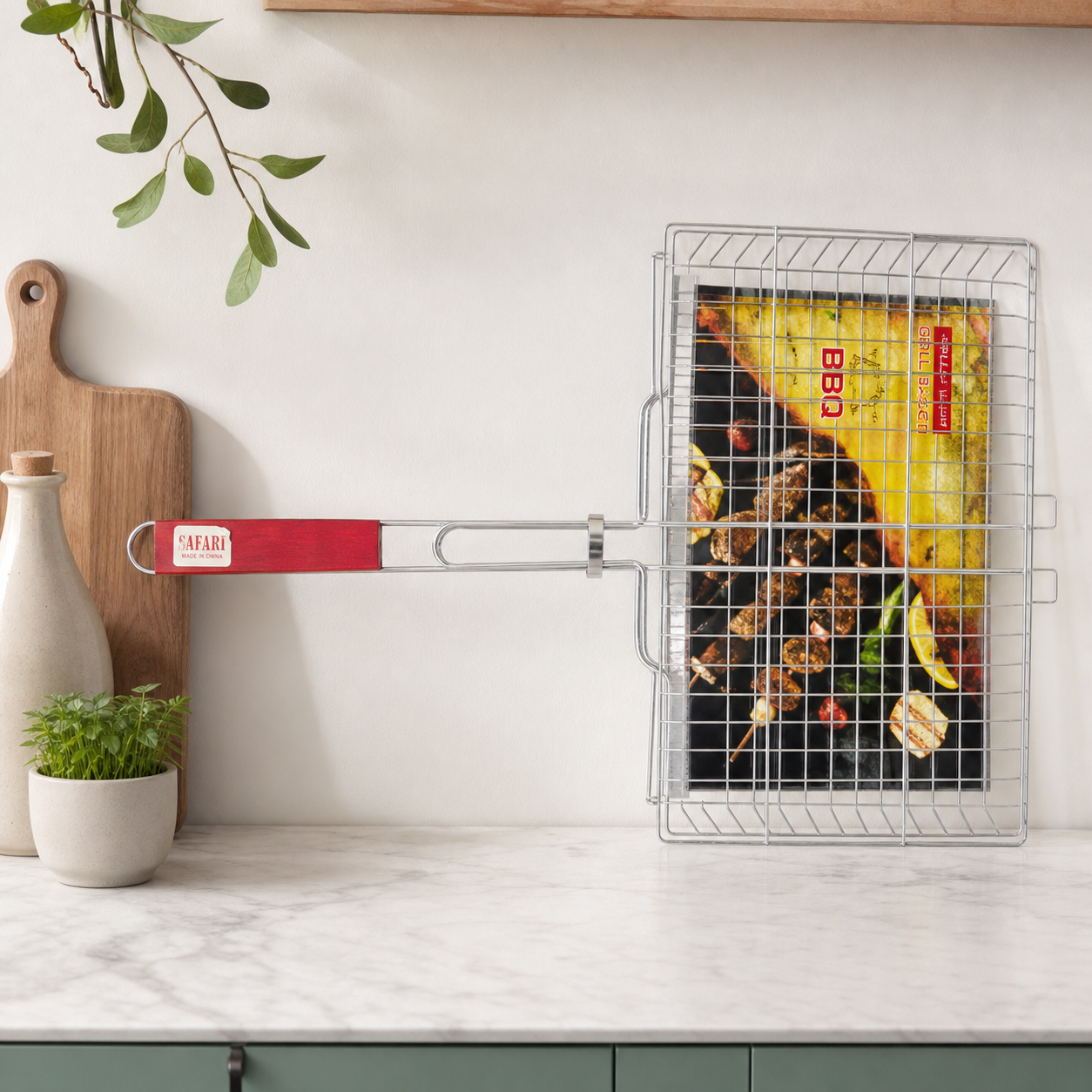 Red-handled steel mesh BBQ basket standing on a kitchen counter, 30 x 55 cm