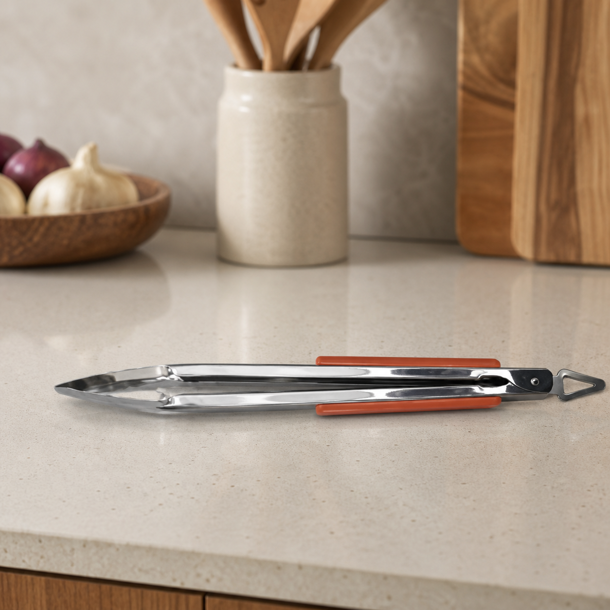Stainless steel BBQ tongs with orange grips resting on a kitchen counter