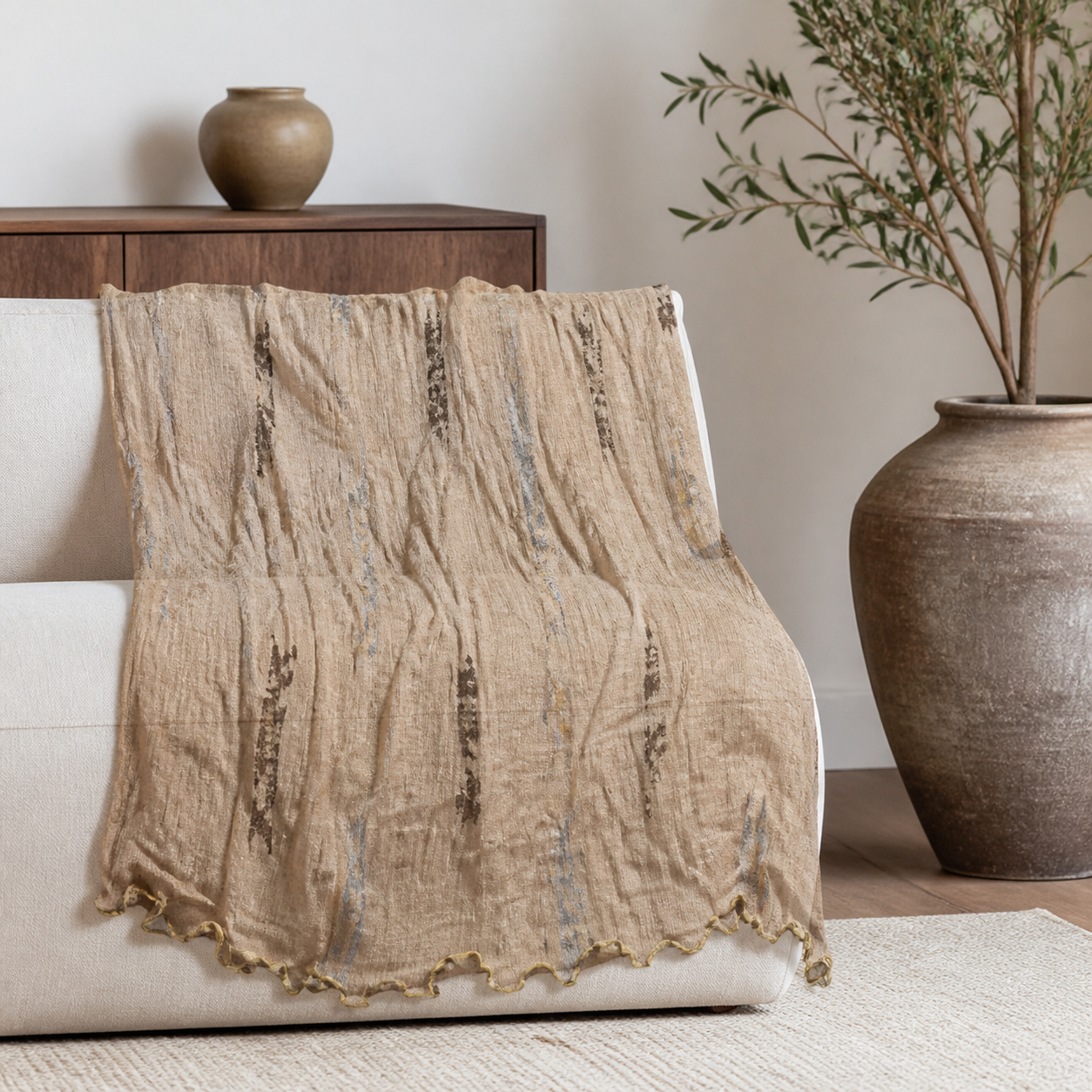 Khaki pleated scarf draped over a cream sofa back, showing its crinkle texture and wavy ruffled hem