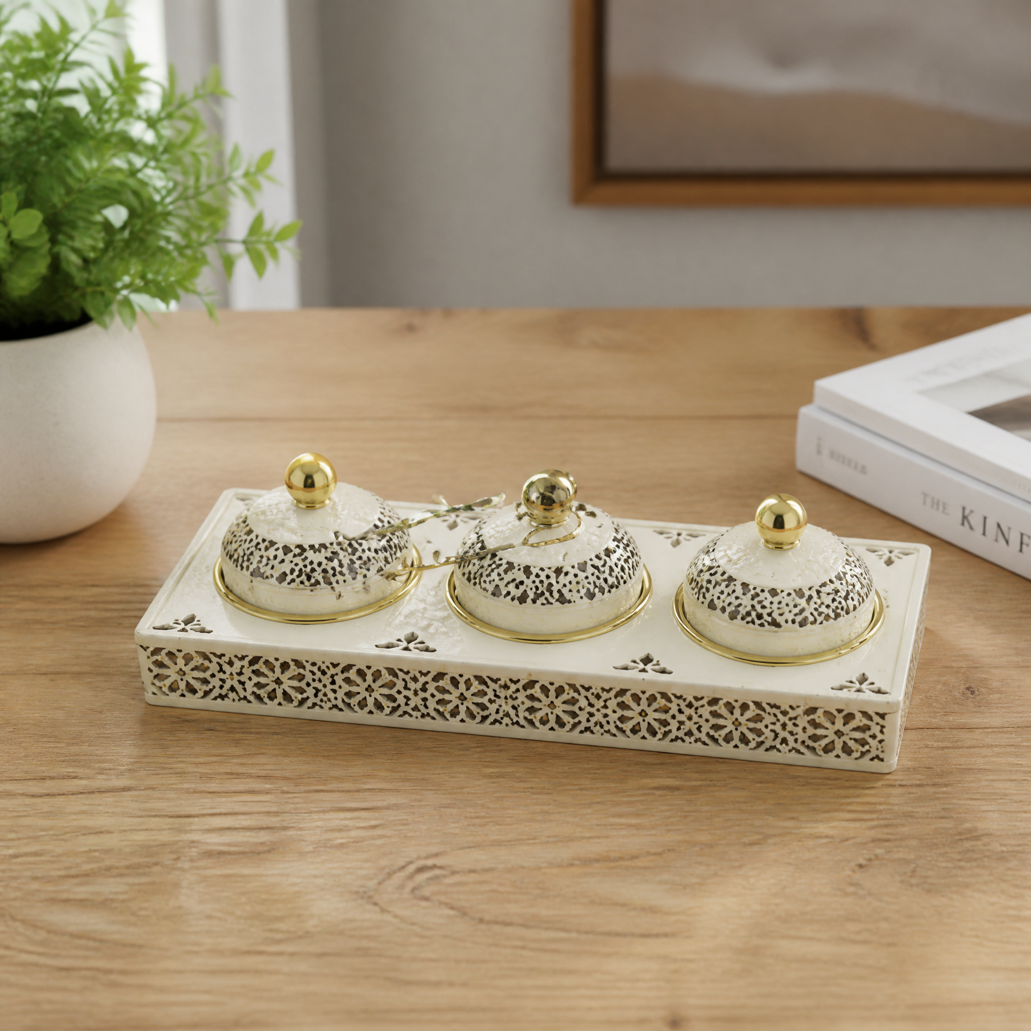 Three-jar ivory and gold candy tray with gold spoons on a wooden table