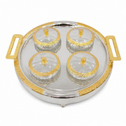 Round silver tray with gold handles holding four clear glass bowls with gold-rimmed glass lids