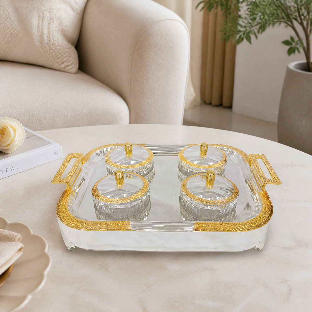 Silver and gold rectangular tray with four lidded glass bowls on a marble coffee table