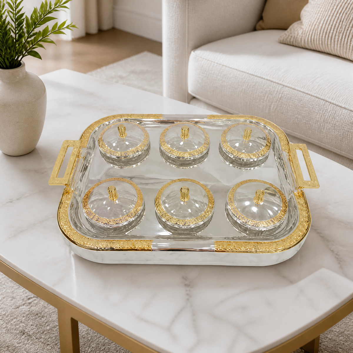 Silver and gold tray with six lidded glass bowls on a white marble coffee table