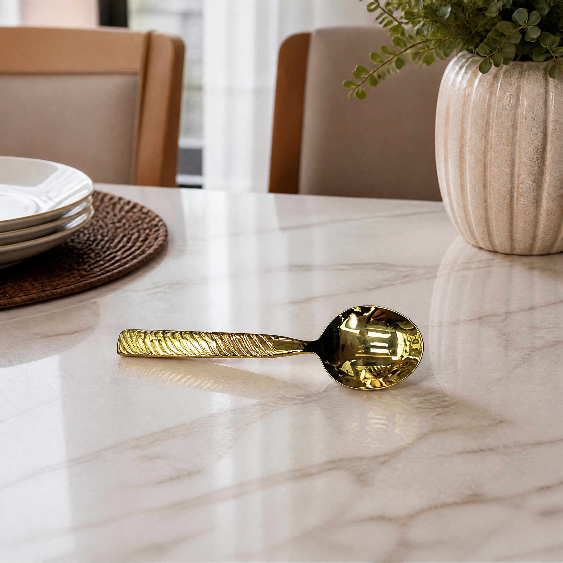 Gold-tone spoon on a marble dining table beside a stack of white plates