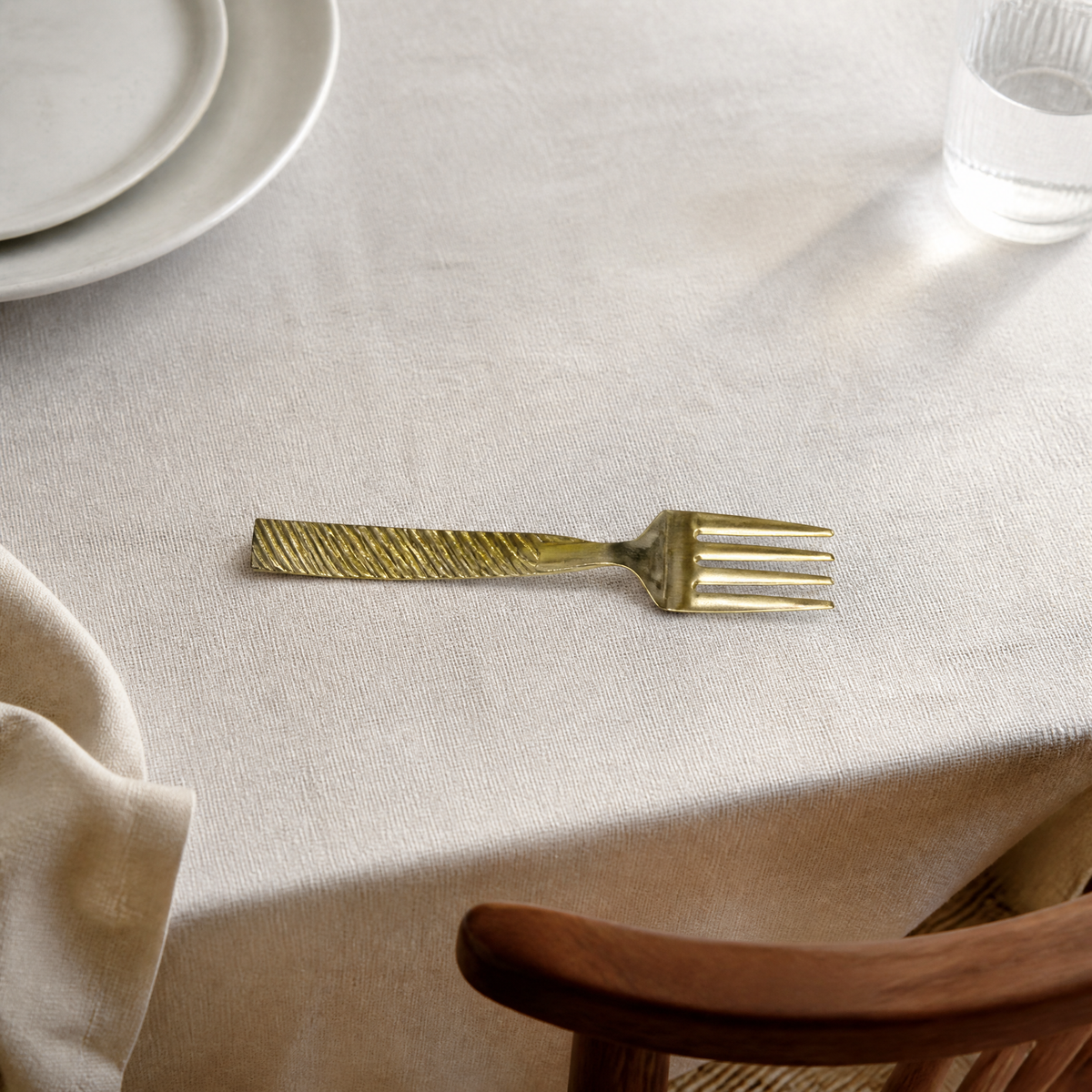 One of six gold-tone dinner forks resting on a linen tablecloth beside a plate