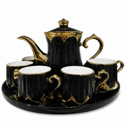 Black and gold tea service with a lidded teapot cups and an oval tray