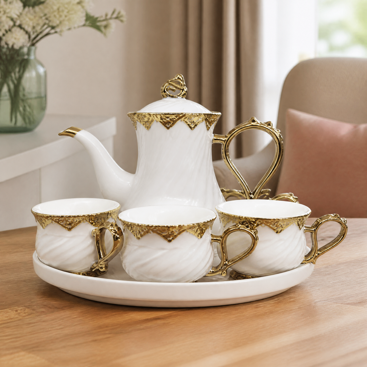 White and gold tea service on a wooden table beside a vase of flowers