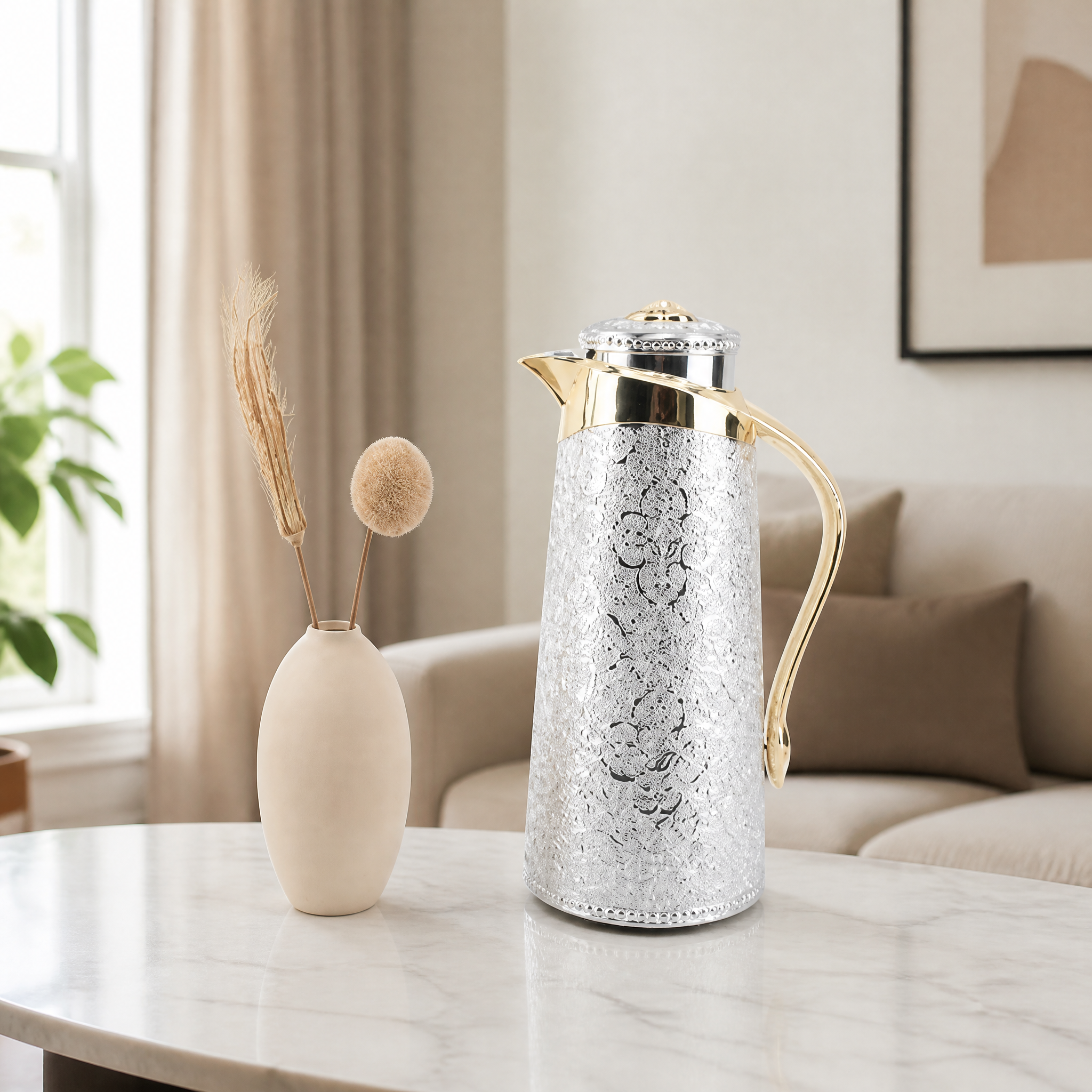 Silver engraved vacuum flask carafe with gold-tone fittings, shown on a marble table