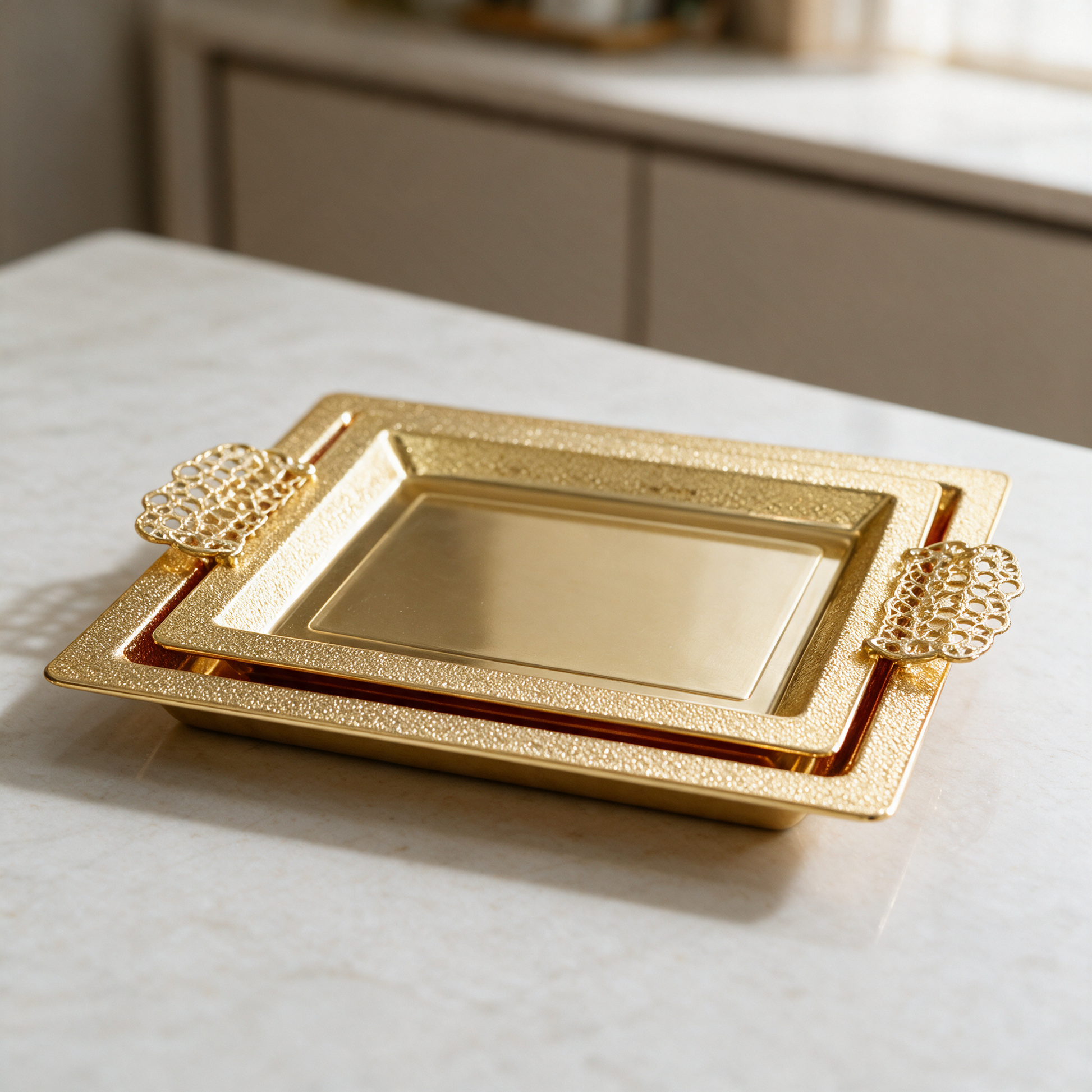 Gold-tone two-piece serving tray set nested on a marble counter, pebbled rims and filigree handles